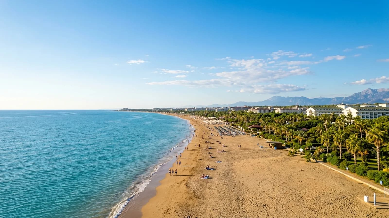 Colakli, Türkiye — the long sandy beach at Colakli near Side, shallow turquoise water and a flat coastal plain of hotel gardens and palms behind.