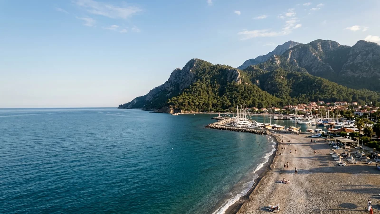 Kemer, Türkiye — the coast at Kemer, a pebble beach and yacht marina where pine-covered Taurus mountains drop almost vertically into a deep blue sea.