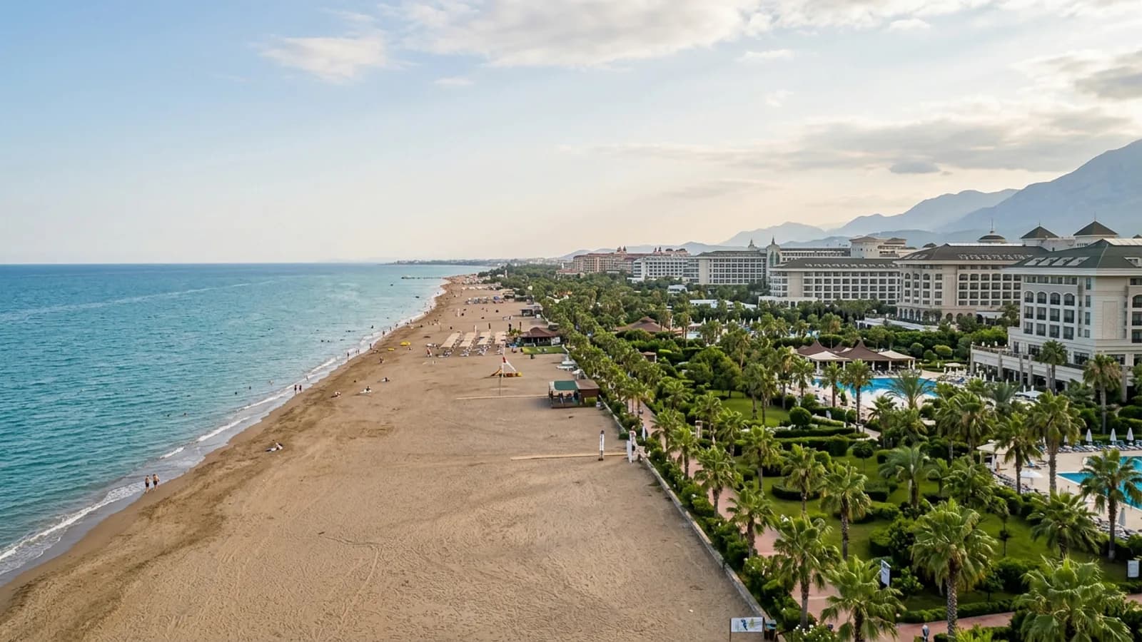 Kundu, Türkiye — the resort strip at Kundu on the coastal plain east of Antalya, a wide sandy beach backed by large hotel gardens and rows of palms.