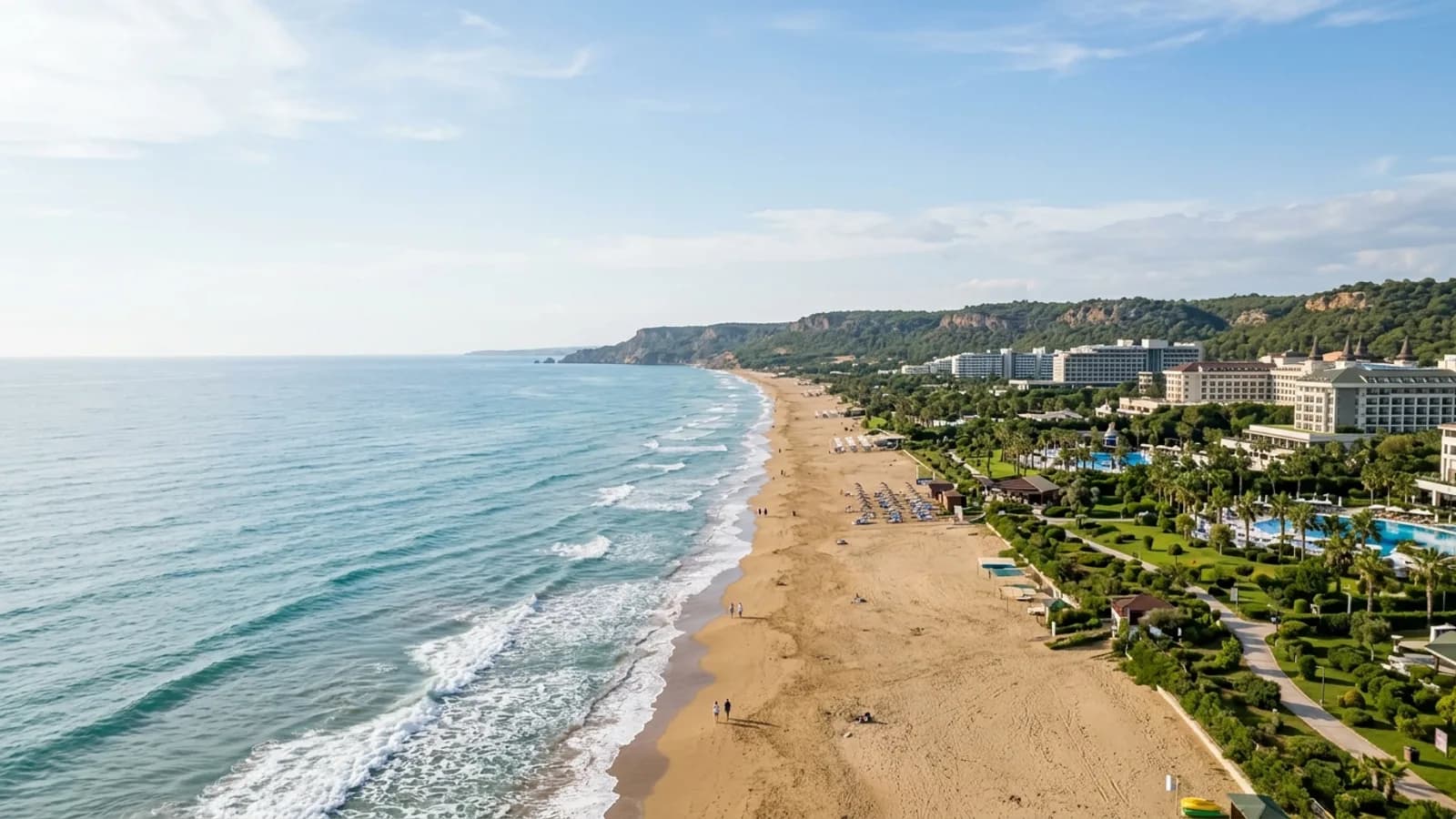 Lara, Türkiye — the long straight sandy beach at Lara east of Antalya, with low cliffs behind the shore and large resort hotels set back among landscaped gardens.