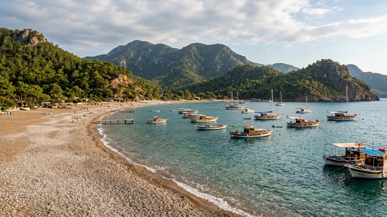 Adrasan, Türkiye — the sheltered bay at Adrasan, a crescent pebble beach with fishing boats moored offshore and pine-covered headlands on both sides.