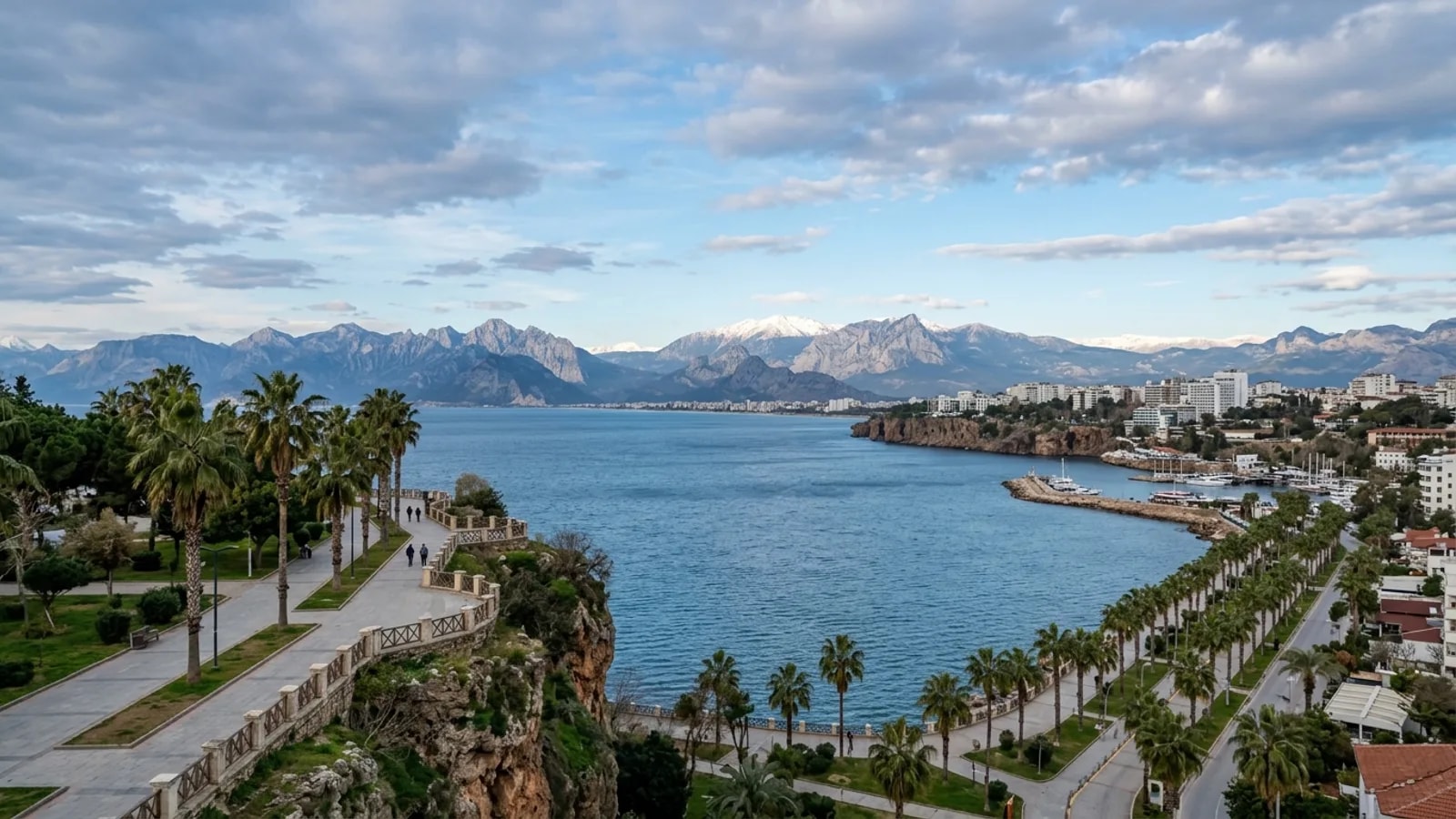 Antalya City Centrum, Türkiye — the modern seafront of Antalya city, palm-lined boulevards on the cliff top and the snow-topped Taurus mountains rising across the bay.