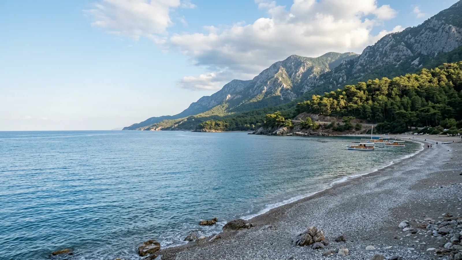 Beldibi, Türkiye — the shore at Beldibi on the Kemer road, a grey pebble beach with pine forest coming down to the water and steep mountain slopes behind.