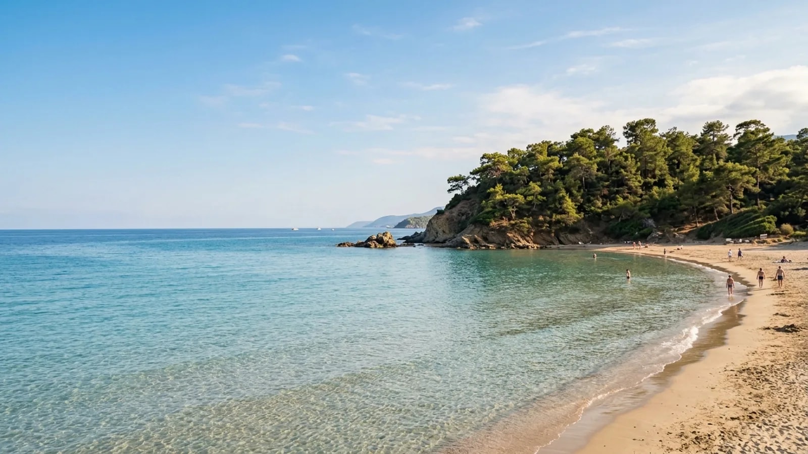 Incekum, Türkiye — the shore at Incekum west of Alanya, a small sandy cove with very shallow clear water and a pine-covered headland to one side.