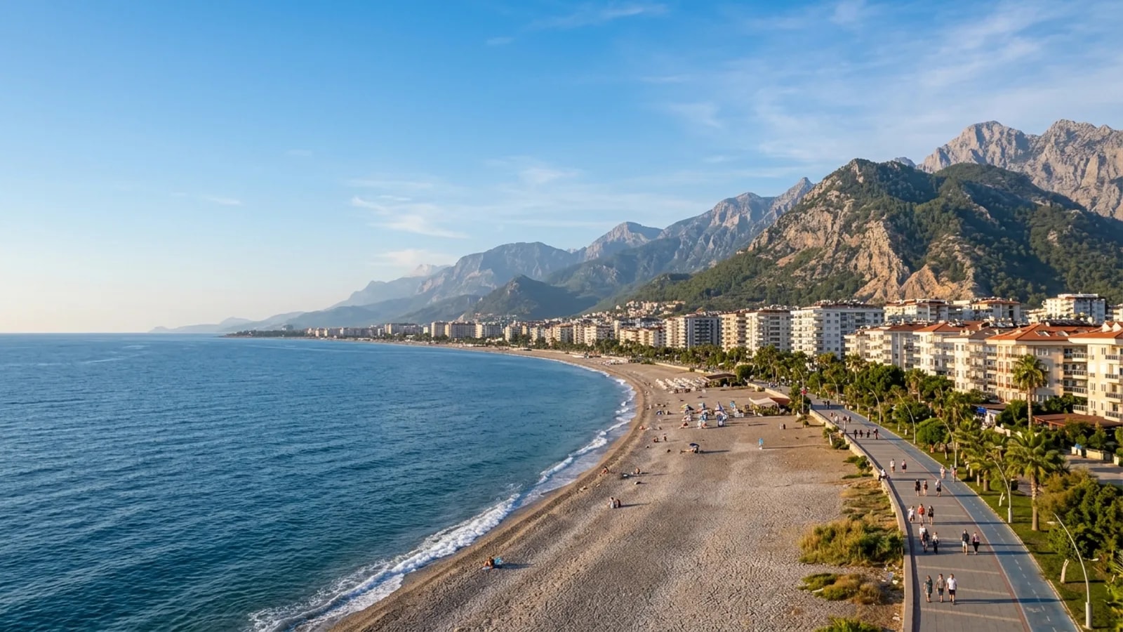 Mahmutlar, Türkiye — the seafront at Mahmutlar east of Alanya, a long pebble shore and promenade below apartment blocks with high mountains behind.