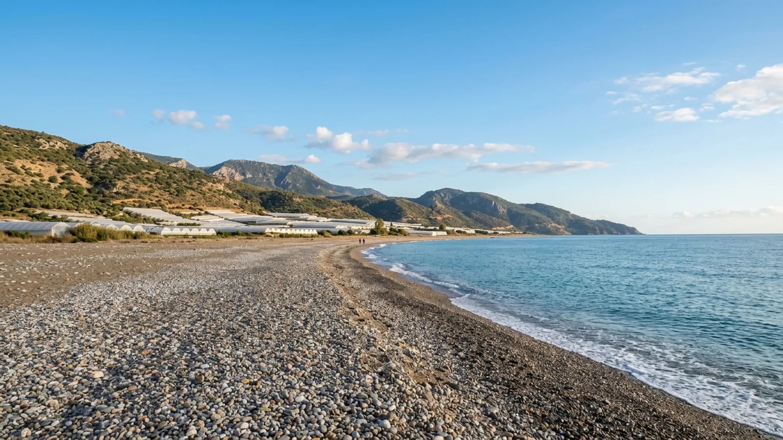 Mavikent, Türkiye — the shore at Mavikent on the coast south of Kumluca, a long quiet pebble beach with greenhouses and hills behind it.