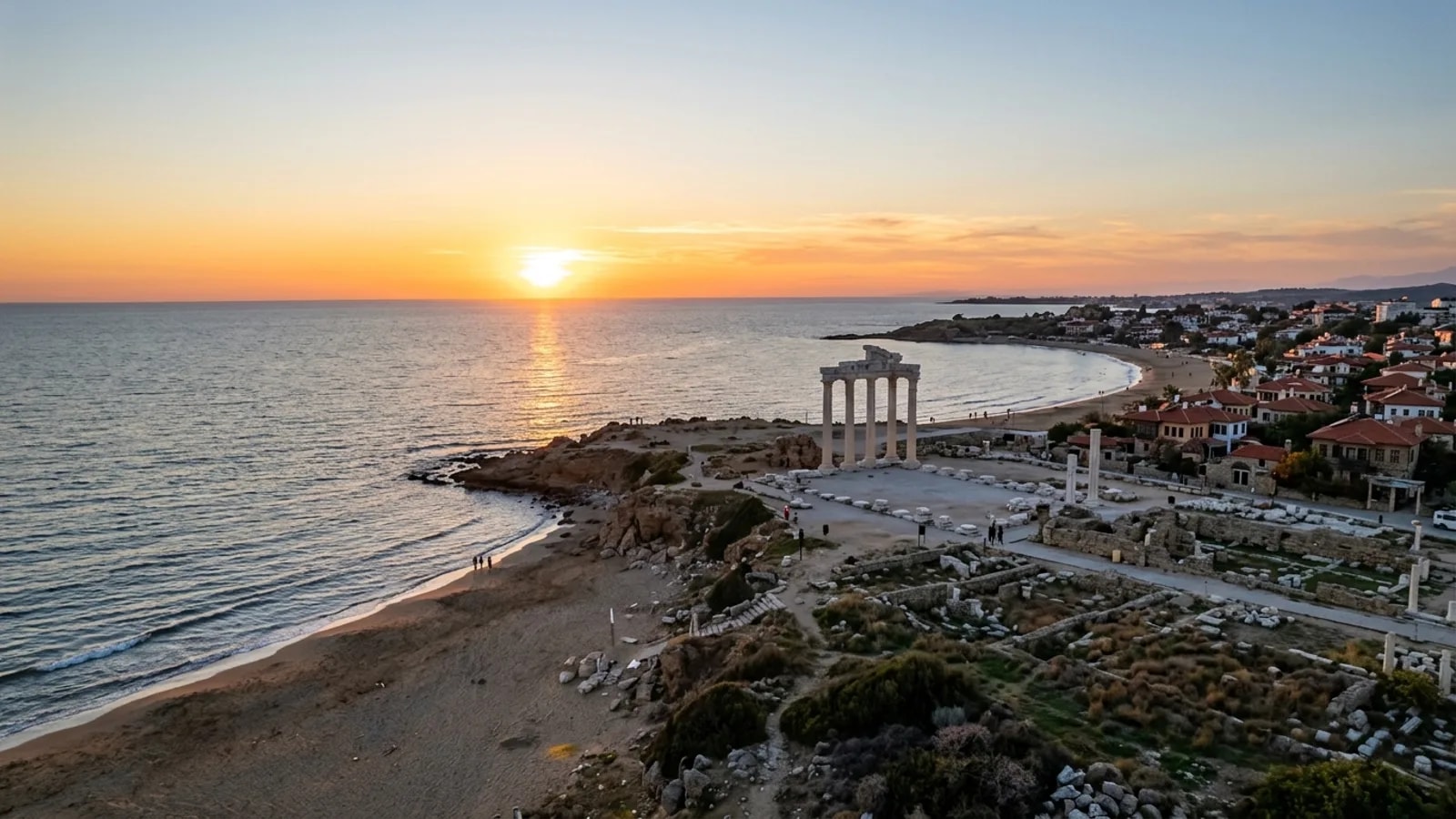 Side, Türkiye — the ancient seaside town of Side, standing marble columns of a Roman temple on a low headland above a sandy beach at sunset.