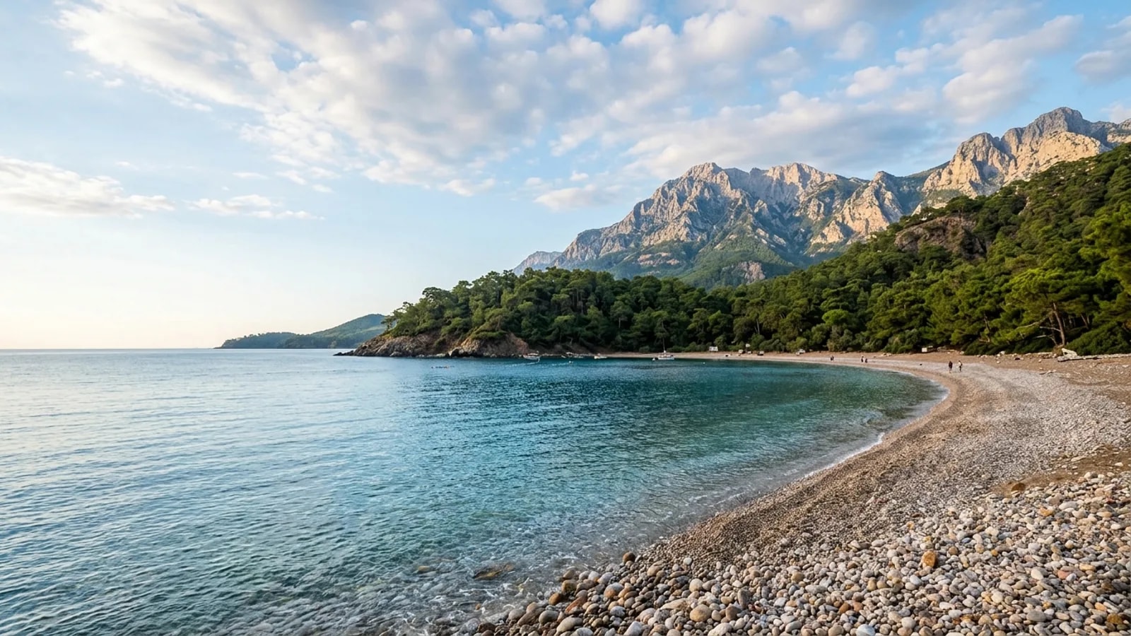 Tekirova, Türkiye — the coast at Tekirova, a sheltered pebble bay ringed by dense pine forest with the high Taurus ridge behind.